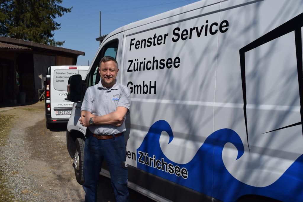 Servicemonteur mit verschränkten Armen vor dem beschrifteten Servicewagen