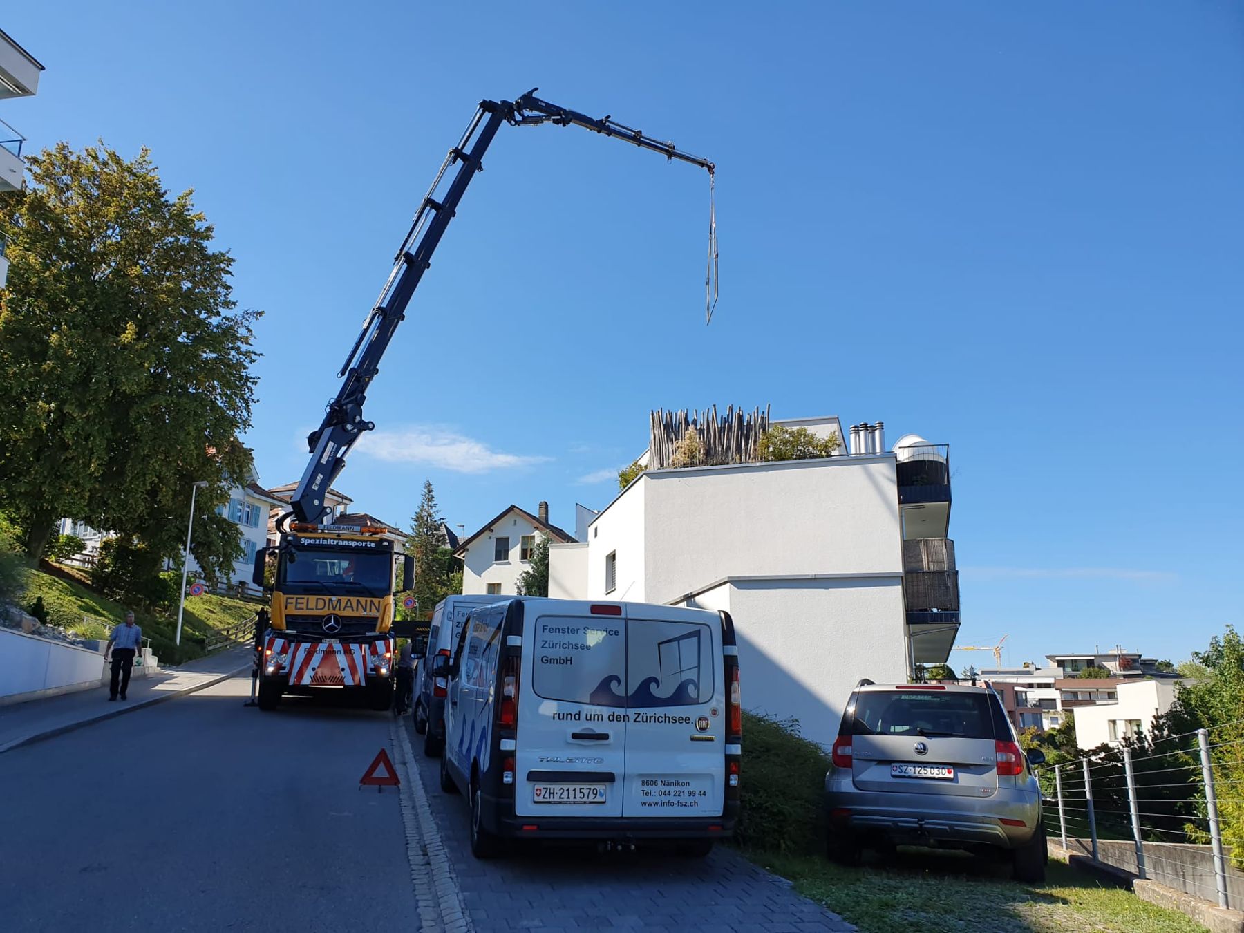 Mobilkran hebt Glas, daneben die Servicewagen von Fenster Service Zürichsee