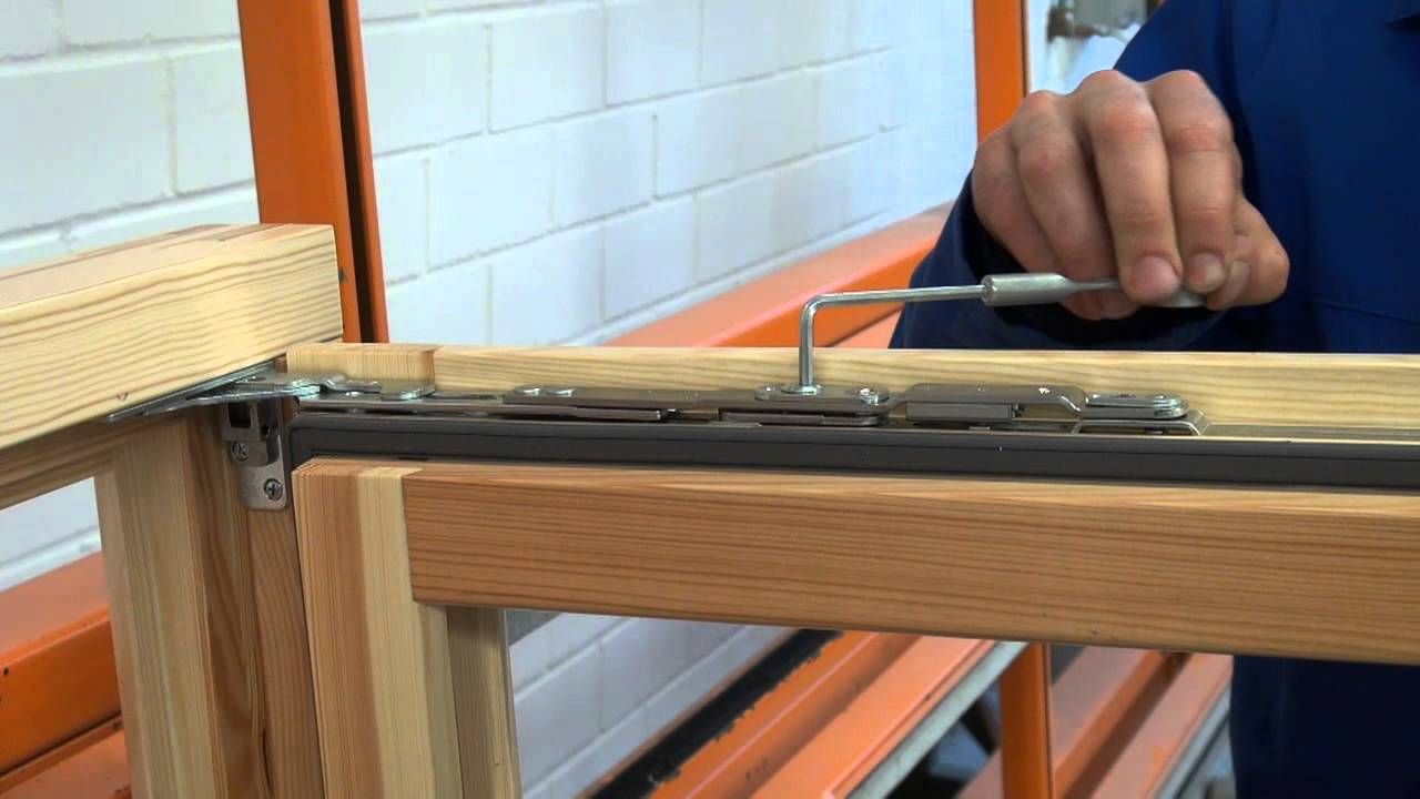 Hand stellt den Beschlag an einem Holzfensterflügel ein